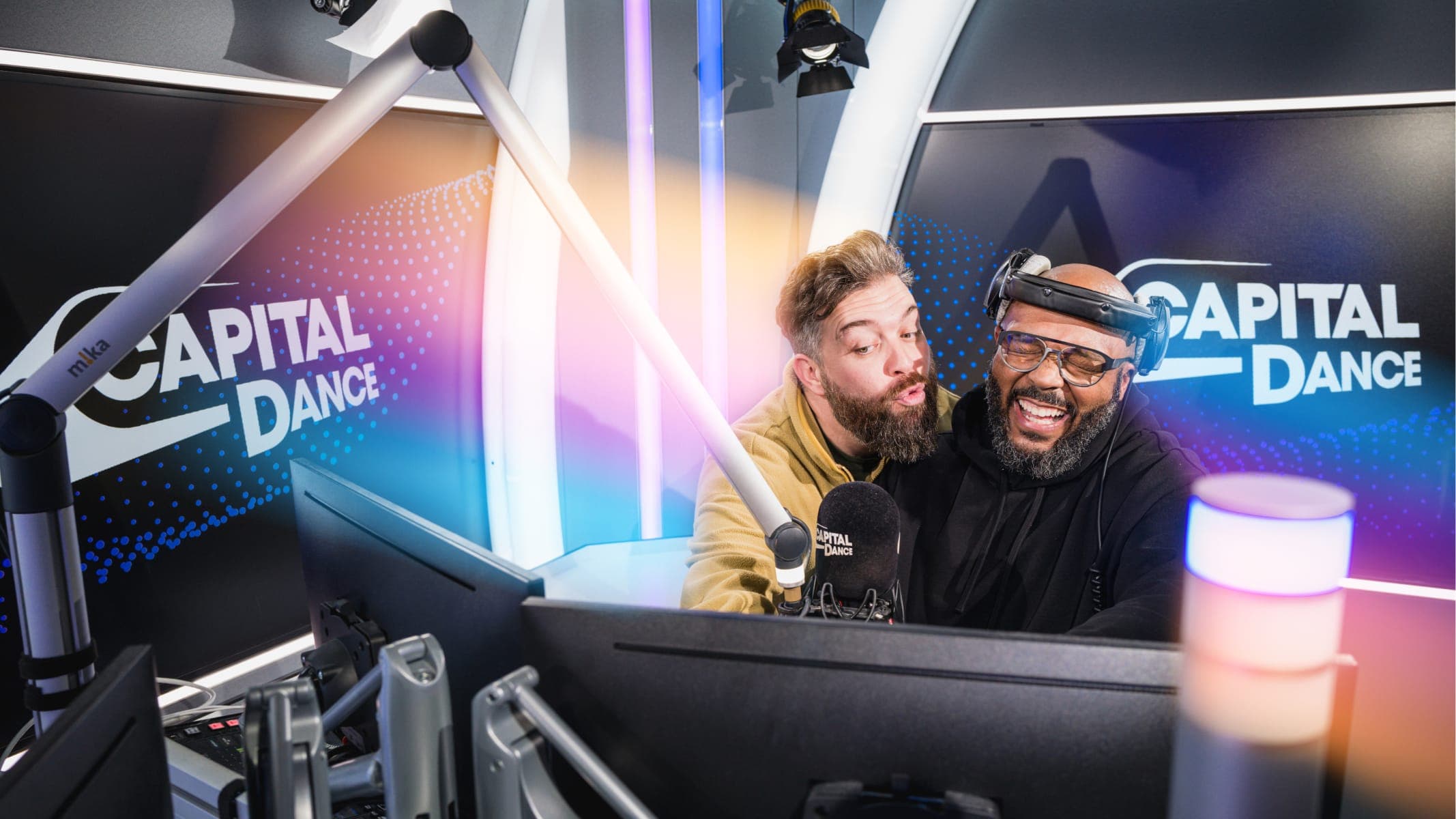 Two radio hosts are in a studio, smiling and interacting with each other. The background displays the Capital Dance logo.