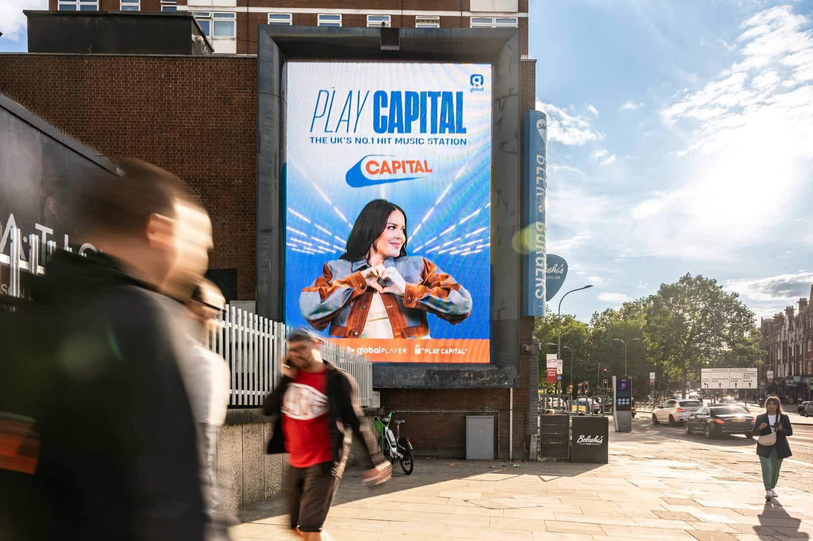 A vibrant billboard promoting Capital station stands tall on a bustling street, catching the attention of passersby.